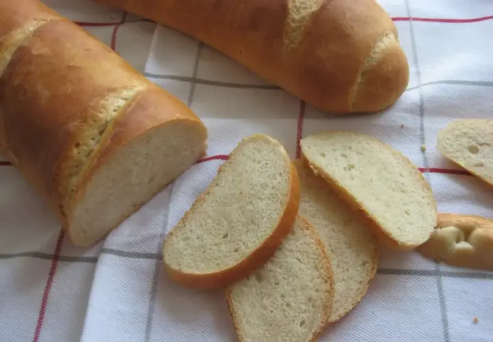 Chleb pszenny na zakwasie, pokrojony w kromki, leży na kratkowanym obrusie. Idealny do śniadania.