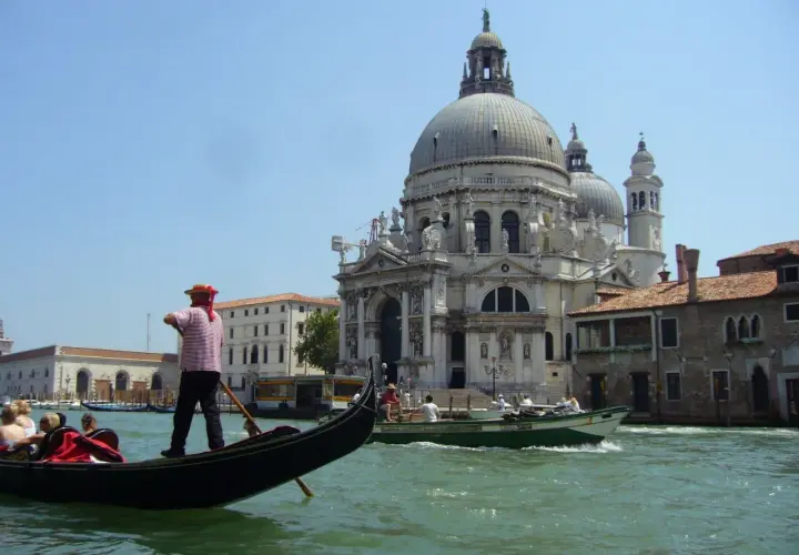 Gondolier wita turystów w Wenecji. W tle Bazylika Santa Maria della Salute i kanał.