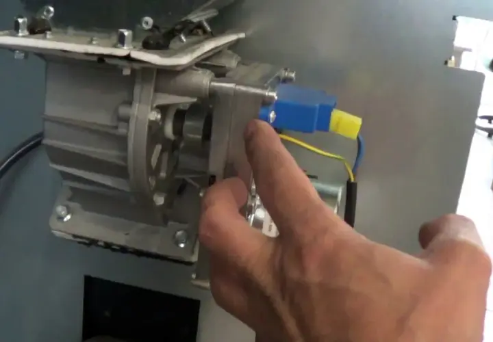 Main d'un homme manipulant le mécanisme d'un poêle à granulés, pour nettoyer le pressostat.