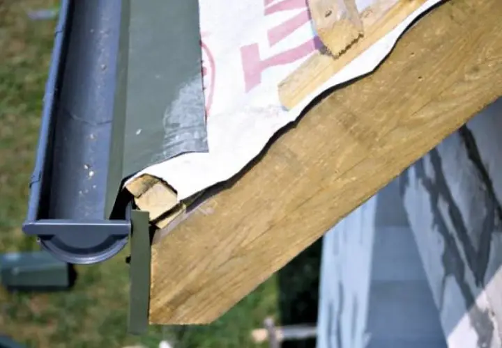 Montaż rynny plastikowej na altanie. Detal mocowania rynny do drewnianej konstrukcji dachu, widoczna membrana dachowa.