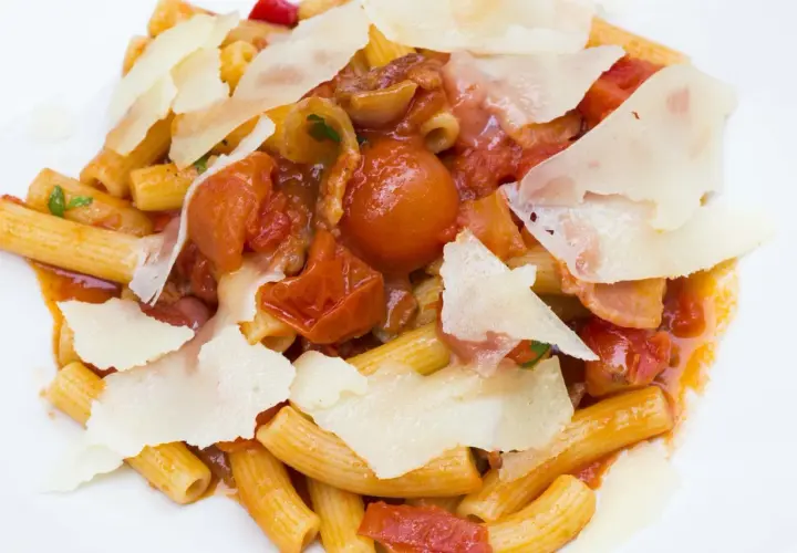 Piatto di rigatoni conditi con un ricco sugo amatriciana, pomodorini, guanciale e scaglie di pecorino.