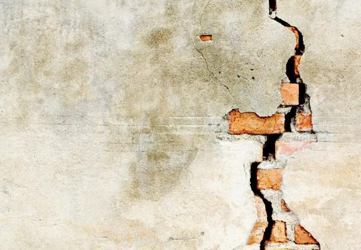 Crepe intonaco interno rivela mattoni rossi. La parete mostra segni del tempo e usura.