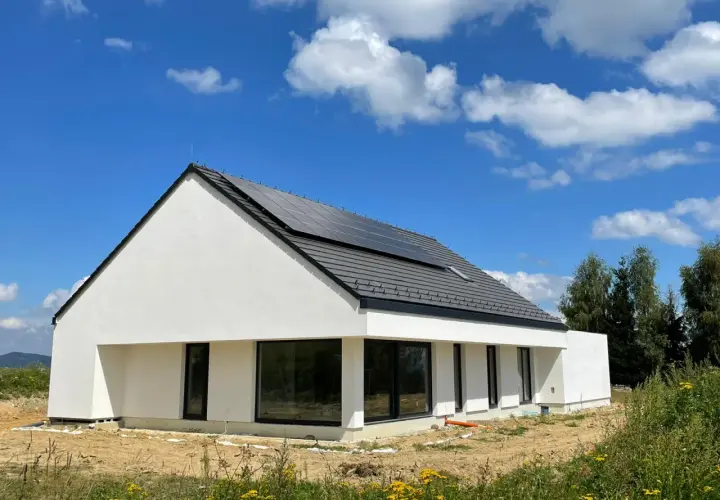 Nowoczesny dom z gotowych elementów betonowych, z panelami słonecznymi na dachu, otoczony zielenią.