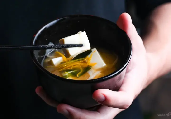 A chopstick lifts a cube of tofu from a bowl of miso soup, showcasing simple yet delicious tofu recipes.