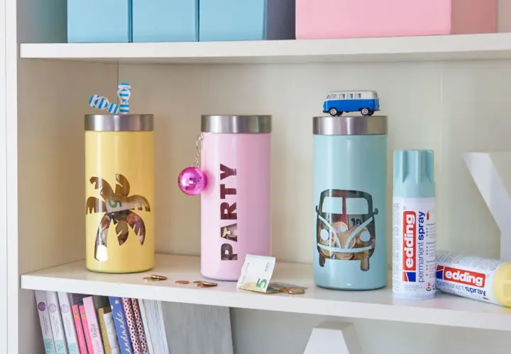 Kolorowe skarbonki DIY z motywami palmy i busa. Na półce obok stoją puszki z farbą w sprayu.