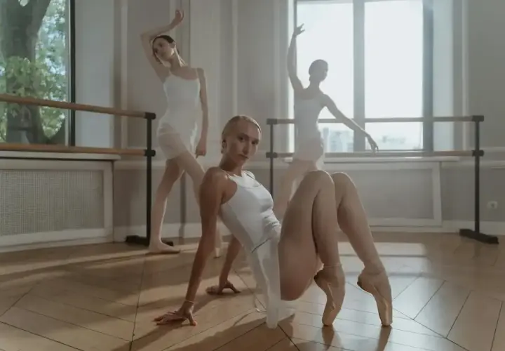 Trzy baletnice w białych strojach tworzą piękną, taneczną figurę na sali baletowej.