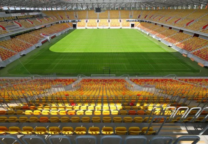Pusta trybuna stadionu Jagiellonii, z żółtymi i czerwonymi siedzeniami, czeka na kibiców. Pojemność stadionu robi wrażenie.