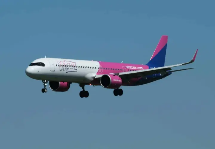 Samolot Wizz Air z różowym i niebieskim ogonem zbliża się do lądowania. Wpisz "gdzie znalezc kod potwierdzenia wizzair" w wyszukiwarkę, aby znaleźć potrzebne informacje.