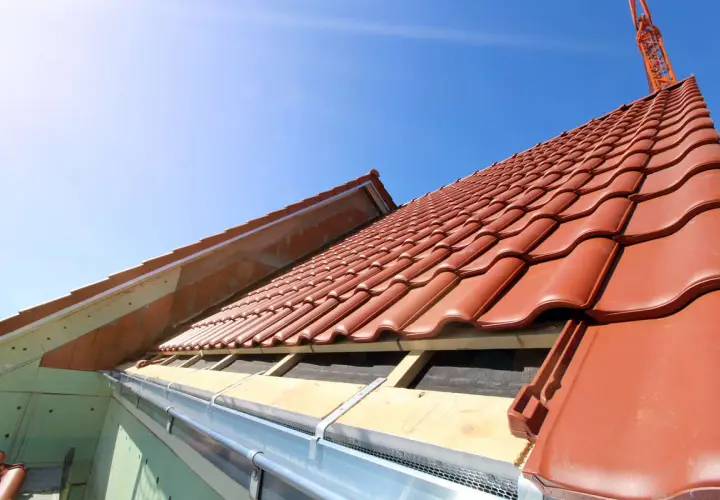 Taktegel i rött läggs på ett hus under uppbyggnad. En kran syns i bakgrunden, redo att lyfta material för framtida byggnadsintegrerade solceller.