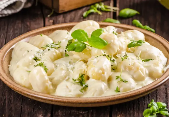 Pyszne gnocchi z kurczakiem w kremowym sosie, udekorowane bazylią i parmezanem, na drewnianym stole.