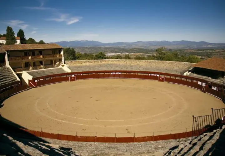 La plaza de toros El Castañar, con su arena de arena y gradas de piedra, se alza majestuosa ante un paisaje montañoso.