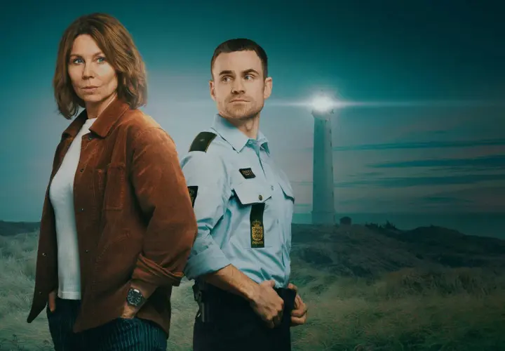 Två poliser står på en kulle med vit sand. I bakgrunden syns ett fyrhus vid havet.