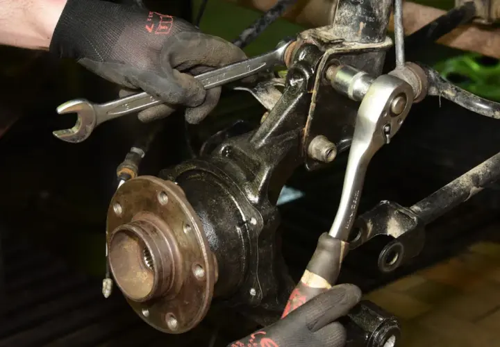 Mechanik w rękawiczkach dokonuje wymiany łożyska koła, używając kluczy do odkręcenia elementów zawieszenia.