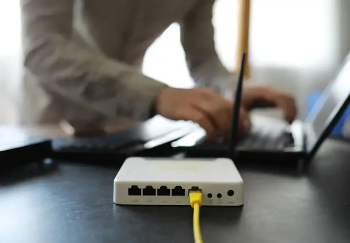 Connexion internet : faut il mettre les espaces pour la clé wifi ? Un routeur blanc est branché, une personne tape sur un ordinateur portable.
