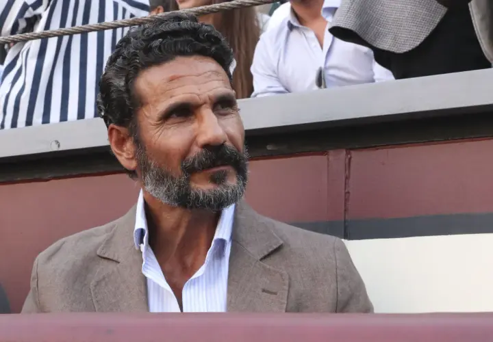 Un torero y actor español, con barba canosa y mirada intensa, viste chaqueta de lino y camisa a rayas.