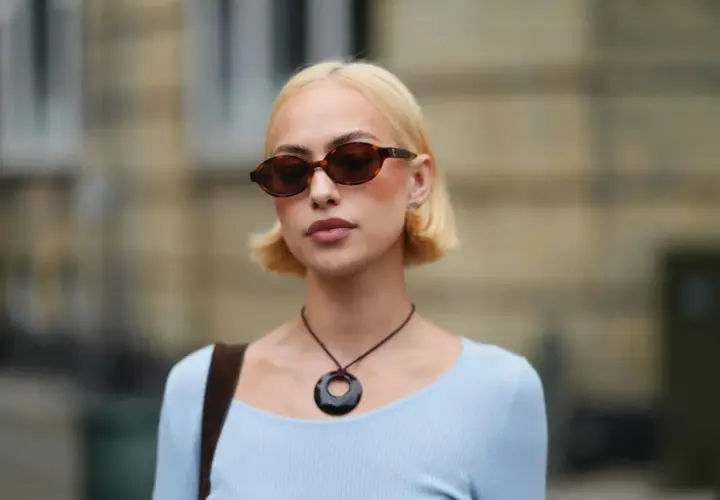 Krótkie fryzury bob w blondzie, stylowe okulary i naszyjnik z okrągłą zawieszką.