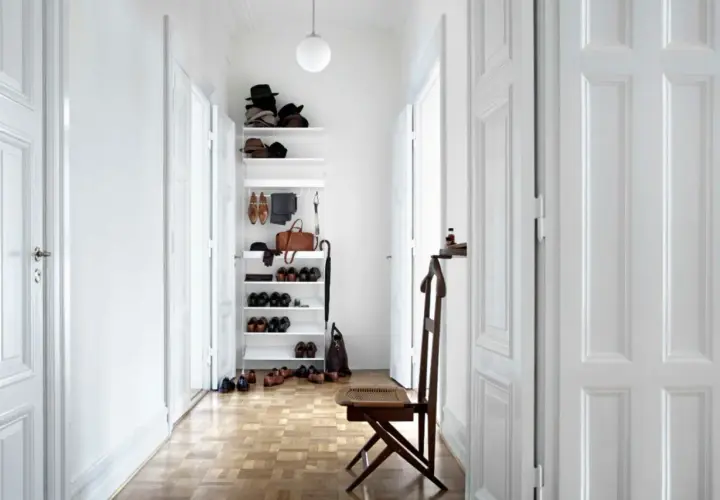 Langer schmaler Flur Ideen: Weißer Regal mit Hüten, Schuhen und Tasche. Holzboden, weiße Türen, Stuhl.