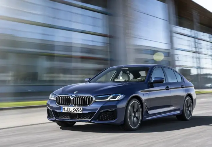 Granatowe BMW G30 540i sunie po drodze, odbijając się w nowoczesnej architekturze.