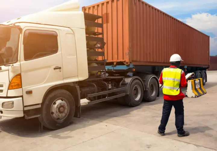 Ein Mann in Warnweste prüft Dokumente neben einem LKW mit Container. Alles bereit für den Frachttransportvertrag.