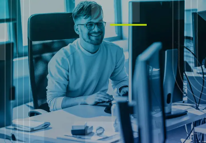 Un homme souriant travaille sur son application bureau, entouré d'écrans d'ordinateur dans un espace moderne.