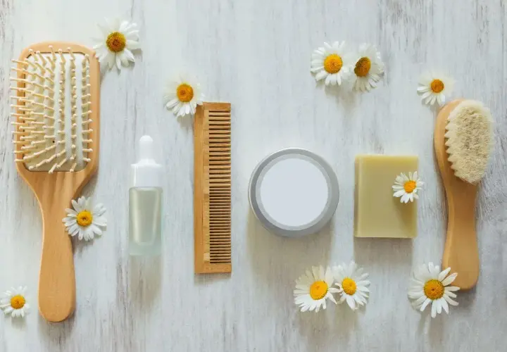 Cepillo, peine, jabón y serum de cuidado personal, todo cruelty free, rodeado de margaritas sobre fondo de madera.