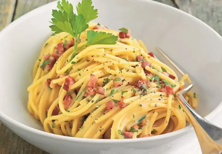 Ein Teller Spaghetti mit cremiger Sauce, Speckwürfeln und Petersilie. Ein Klassiker: Schinken Carbonara.