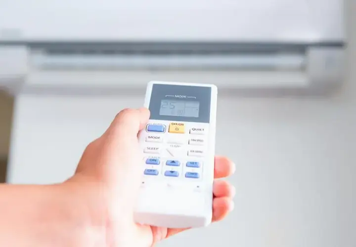 Mano sujetando control remoto de aire acondicionado, ajustando el modo calor a 25 grados.