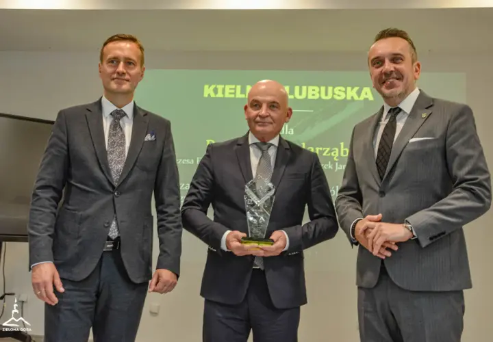 Trzech mężczyzn w garniturach pozuje do zdjęcia, jeden z nich trzyma statuetkę.