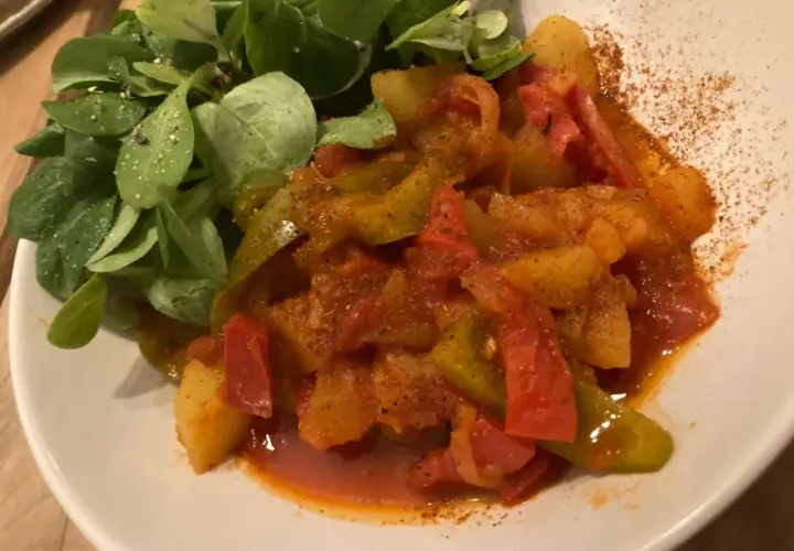 Un plat coloré de poivrons et pommes de terre mijotés, servi avec une salade verte. Une recette simple et savoureuse.