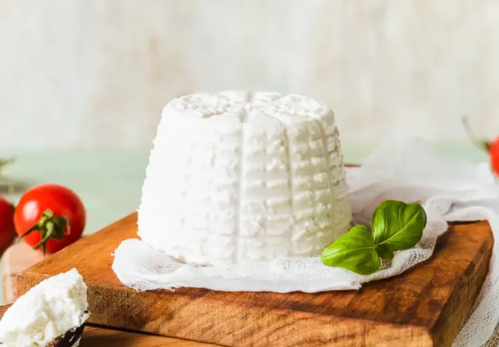 Świeża ricotta na desce, obok pomidorki i bazylia. Idealny składnik do lekkich dań.