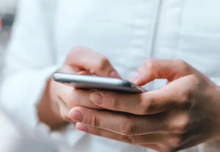 Dłonie trzymające smartfon, uważaj na oszustwa typu smishing, które mogą przyjść w każdej chwili.