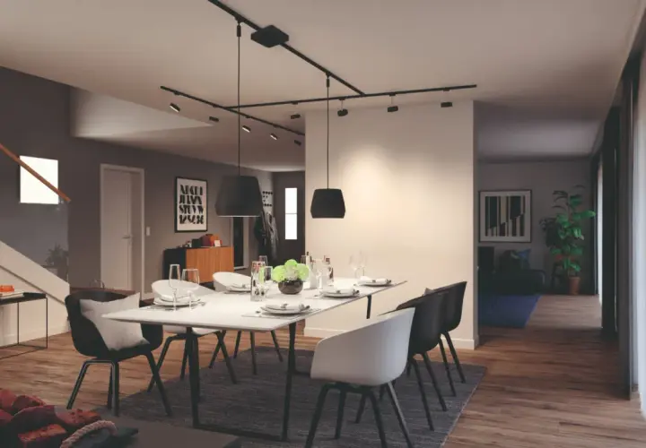 Nowoczesny salon z jadalnią, gdzie centralnym punktem jest stół z krzesłami, a nad nim elegancki system oświetlenia szynowego.