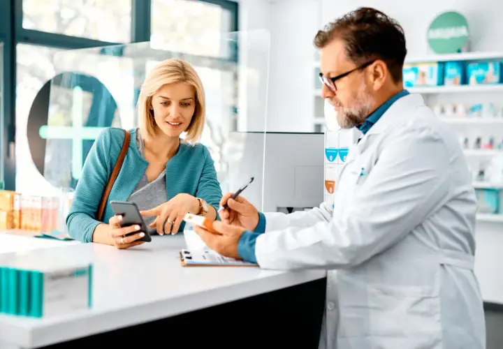 Farmacista spiega a cliente un esempio di farmaci off-label, mostrando una scatola e consultando il telefono.