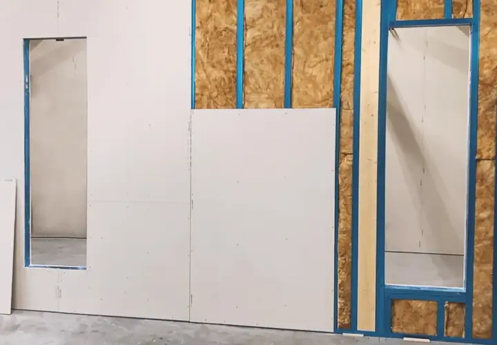 Fase iniziale di come fare una parete in cartongesso: pannelli bianchi fissati su struttura metallica blu, con isolamento visibile.