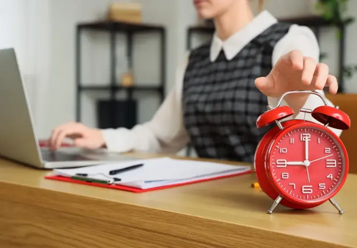 Kobieta wyłącza budzik, pracując przy laptopie. Czyżby to początek dnia w modelu 4 dniowy tydzień pracy?