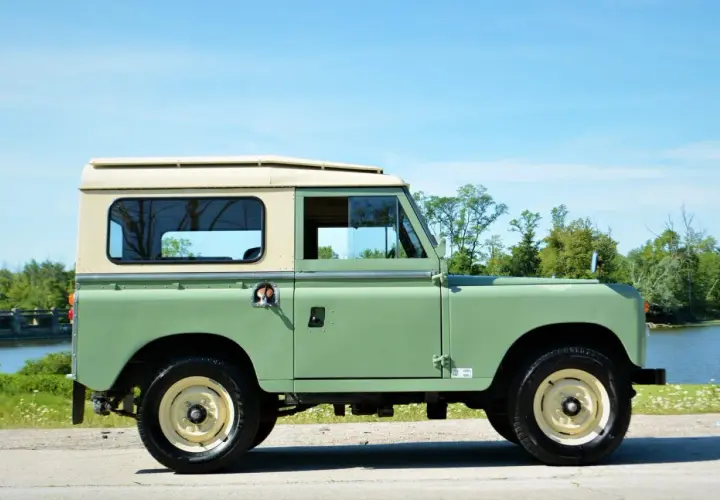 Land Rover Santana verde y crema, listo para una aventura todoterreno junto a un lago.