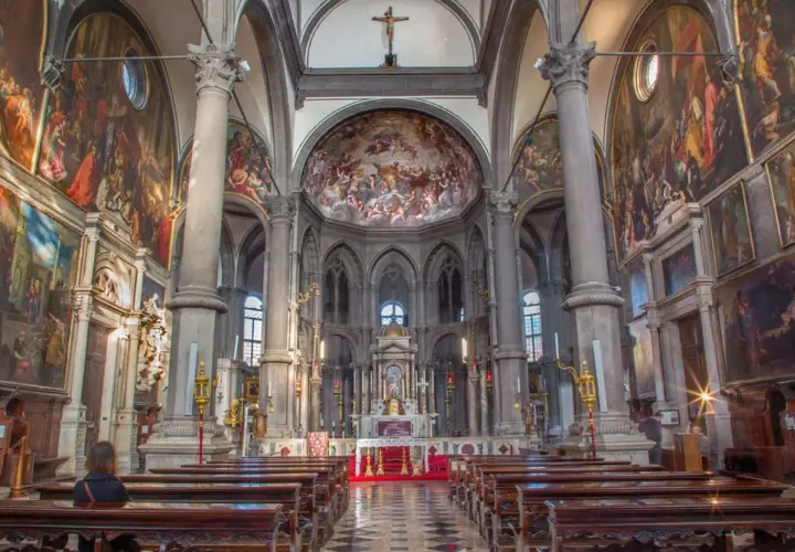Intérieur de San Zaccaria à Venise, avec des fresques grandioses, des colonnes imposantes et des bancs en bois.