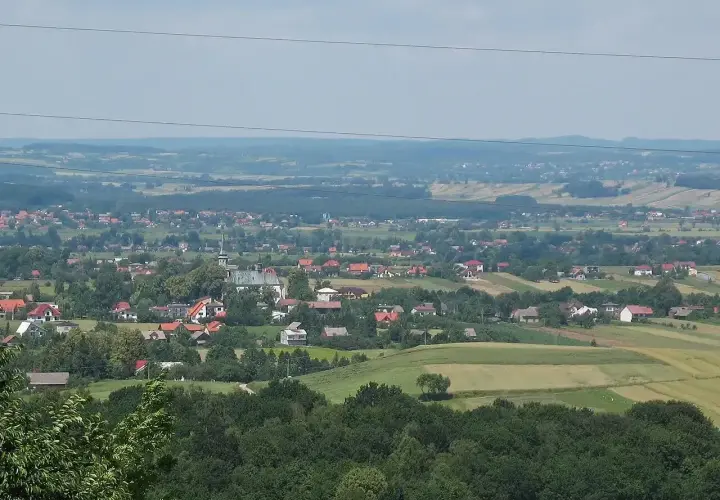 Widok na malowniczą wieś Przytkowice z kościołem w centrum, otoczoną zielonymi wzgórzami i polami.
