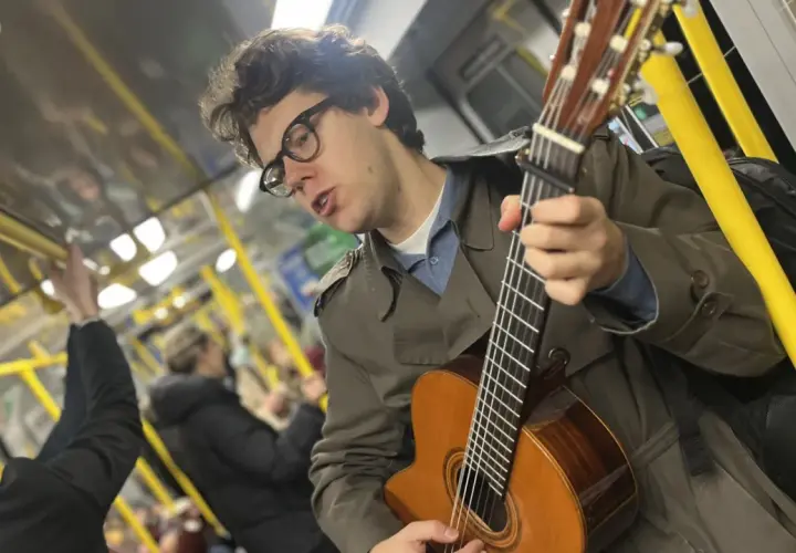 En ung man med glasögon spelar gitarr på tunnelbanan, en musikalisk själ med stockholm roots.