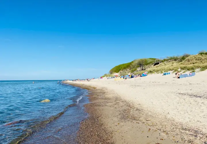 Sonniger Tag am Strand Nonnevitz. Menschen entspannen sich unter bunten Schirmen, während sanfte Wellen das Ufer erreichen.