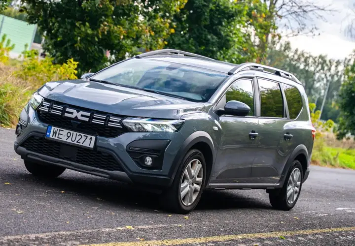 Szare auto 7 osobowe Dacia Jogger na tle zieleni. Idealne na rodzinne wycieczki.