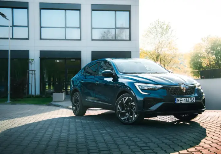 Elegancki, granatowy Renault Arkana na tle nowoczesnego budynku. Sprawdź, jaka jest jego renault arkana cena i możliwości.