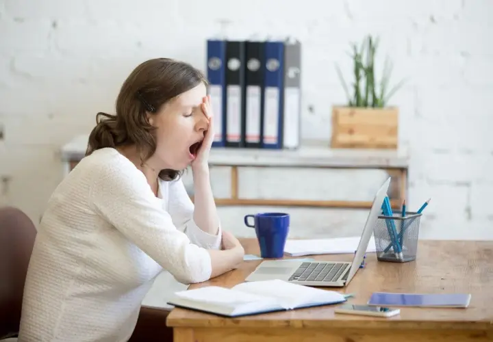 Donna al lavoro, con sbadigli continui, forse per l'ansia o la stanchezza. Sul tavolo, laptop, tazza blu e quaderni.