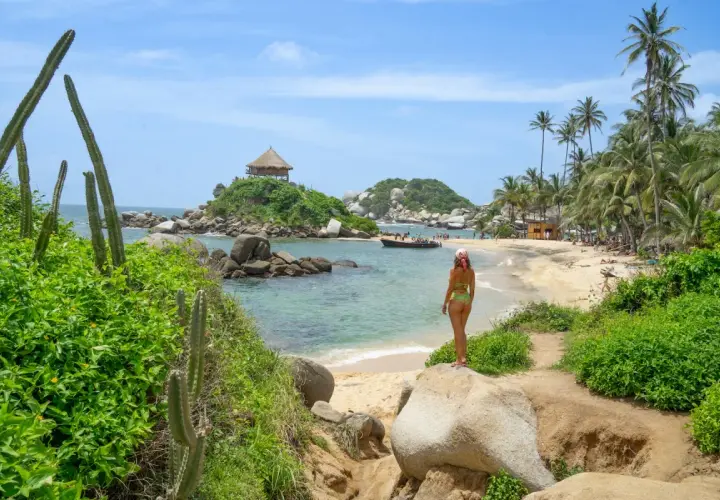 Mujer en bikini admira una playa paradisíaca con palmeras y un kiosko en una isla, ideal para un viaje a Colombia.