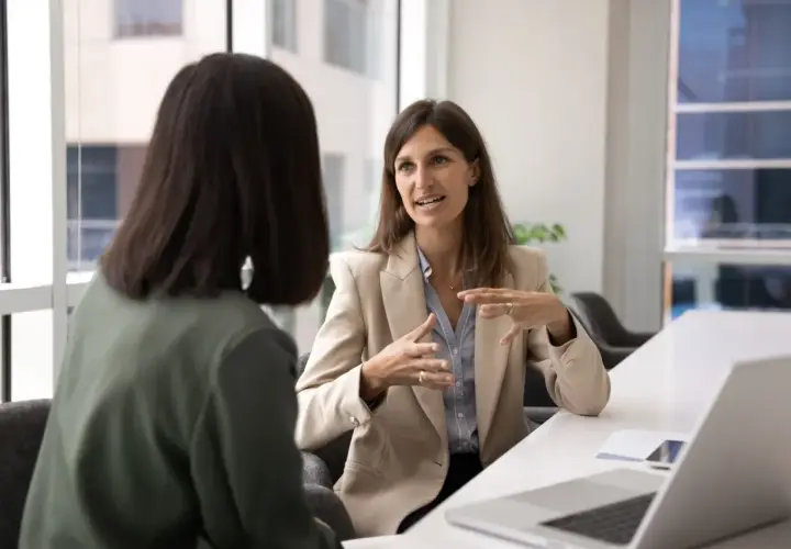 Two women in a meeting. One explains a concept, perhaps what OCB is, with animated hand gestures.