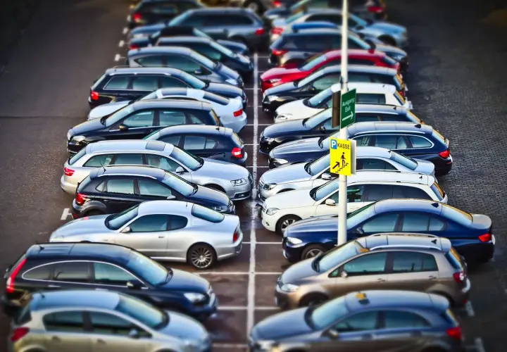 Rząd samochodów na parkingu. Znak "Kasse" sugeruje, że to parking płatny. KNF co to? To może być skrót od nazwy firmy zarządzającej parkingiem.