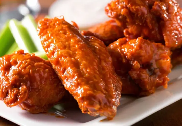 Un plato de alitas de pollo bañadas en salsa picante, acompañadas de bastones de apio fresco. ¡Un clásico irresistible!