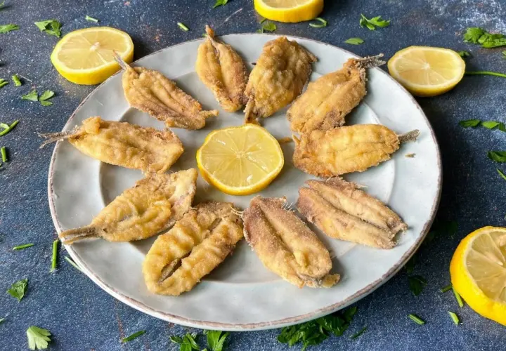 Bocartes fritos crujientes y dorados, servidos en un plato con rodajas de limón y perejil fresco. ¡Un manjar listo para disfrutar!