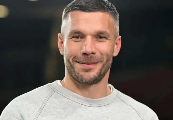 Uśmiechnięty Lukas Podolski w szarej bluzie. Jego kariera piłkarska i biznesowa zbudowały imponujący majątek.