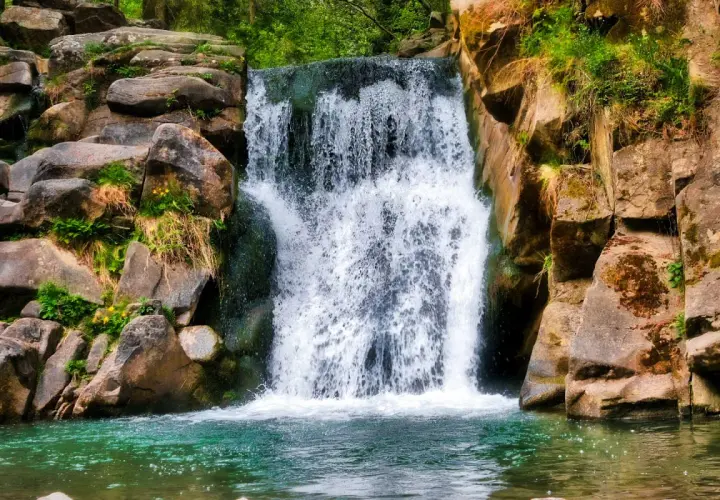 Wodospad w skalistej scenerii, idealny cel dla miłośników **best waterfall hikes**. Zielona woda i bujna roślinność.